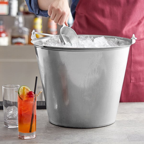 A person stirring ice in a Vollrath stainless steel dairy bucket filled with drinks.