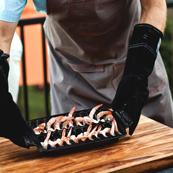 A man in a black apron holding a tray of shrimp grilled in an Outset cast iron pan.