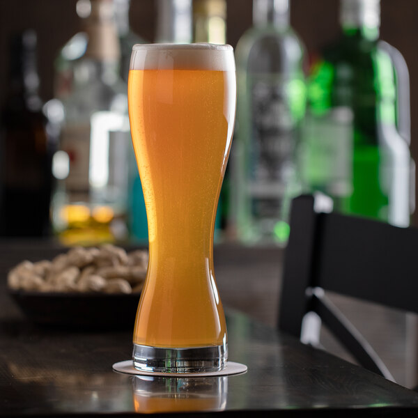 A Stolzle wheat beer glass full of beer on a table.