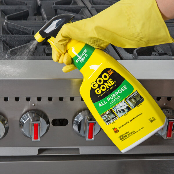 A gloved hand sprays Goo Gone All Purpose Cleaner on a stove.