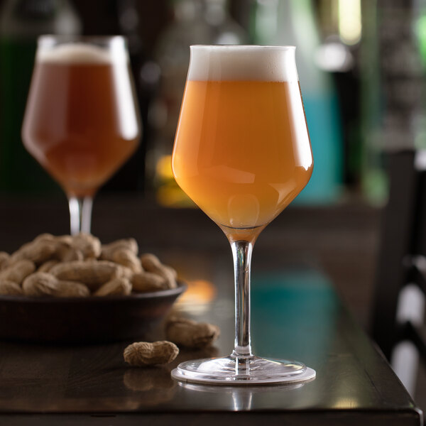 A Stolzle stemmed beer glass filled with beer on a table with peanuts.