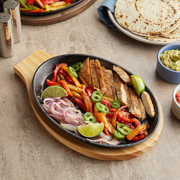 A Choice oval cast iron fajita skillet with meat and vegetables on it.