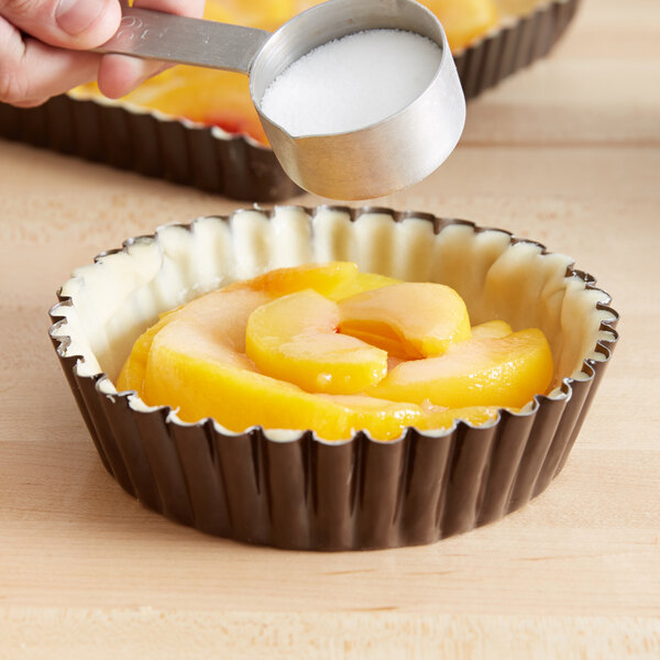 A person pouring sugar into a tart using a Gobel fluted deep tart pan.