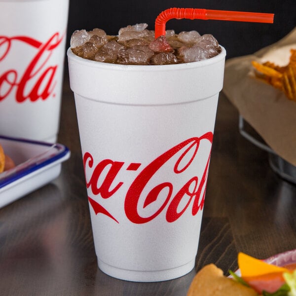 A Dart white foam cup with red Coca-Cola text filled with ice and a straw.