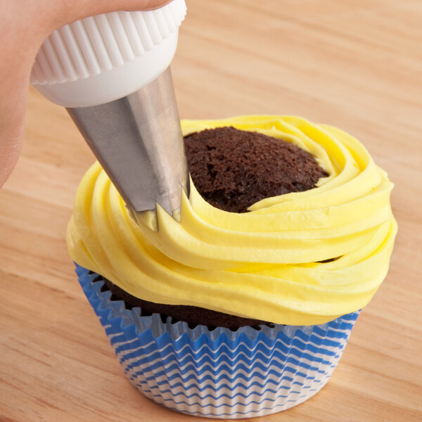 A hand using an Ateco open star piping tip to pipe yellow frosting onto a cupcake.
