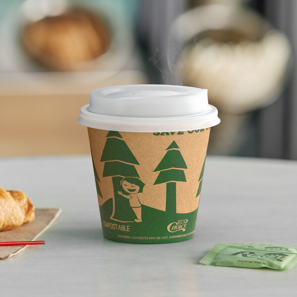 An EcoChoice Kraft paper hot cup with a tree design and a white lid on a table with a croissant.