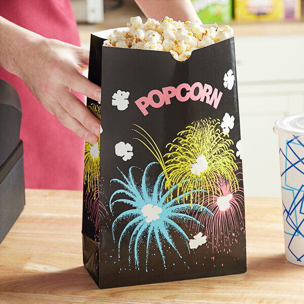 A person holding a Bagcraft Funburst Design popcorn bag with fireworks on it.