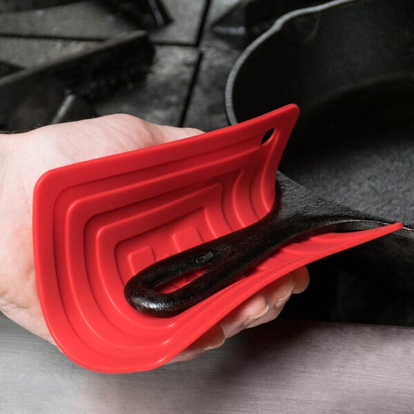 A hand holding a red Lodge silicone pot holder over a red and black spatula.