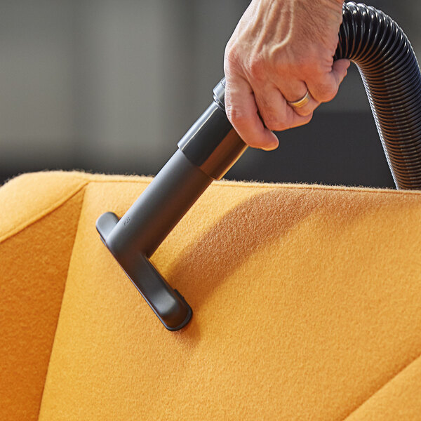 A hand using a Lavex upholstery tool attached to a black tube on a couch to vacuum.