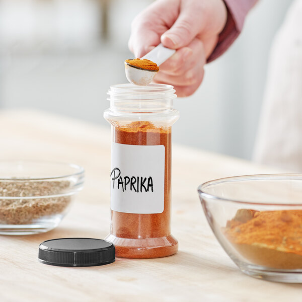 A person pouring red spice into a round plastic spice jar.