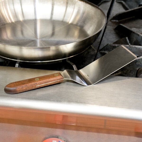 A Victorinox wood-handled solid grill turner in a silver pan.