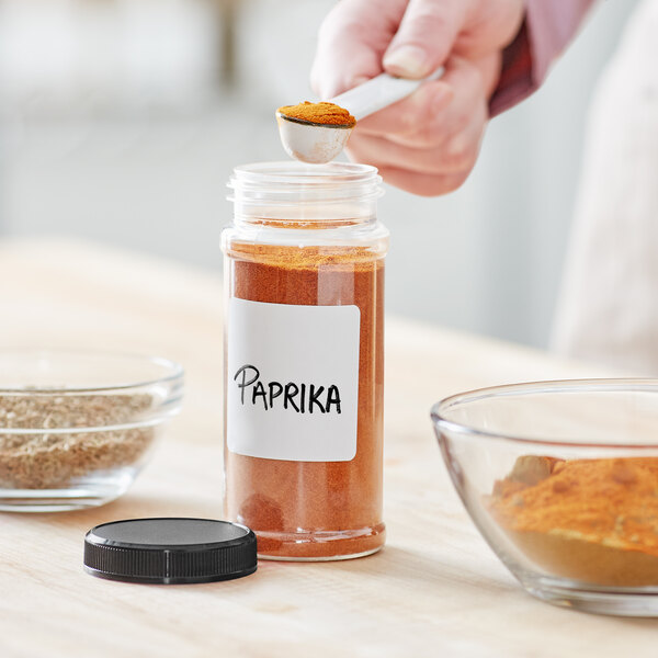 A person pouring paprika into a 53/485 Round Plastic Spice Container.