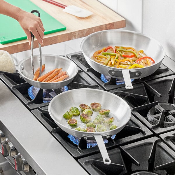 A person cooking vegetables in Choice aluminum frying pans on a stove.