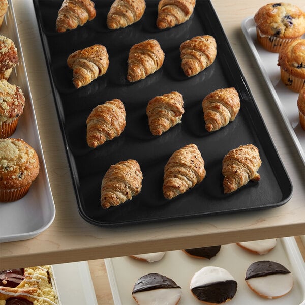 A black Cambro market tray of pastries and muffins on a counter in a bakery display.