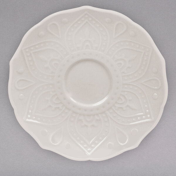 A close up of a white 10 Strawberry Street Dahlia saucer with a flower design on it.