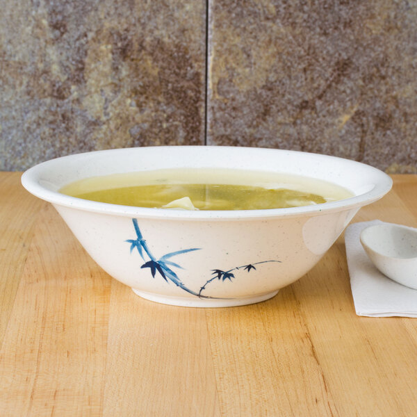A blue and white Thunder Group Blue Bamboo melamine bowl filled with soup on a table with a spoon.