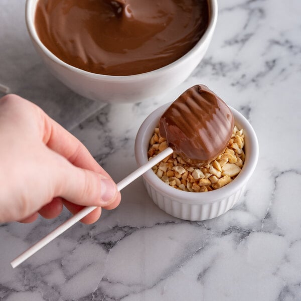 A hand holding a Paper Lollipop Stick with a chocolate covered marshmallow in a bowl of chocolate.