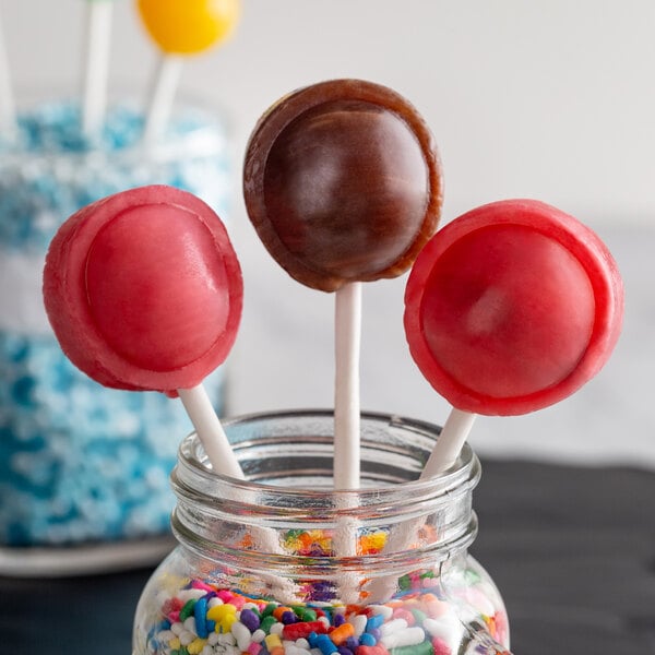 Three paper lollipop sticks in a jar with colorful sprinkles.