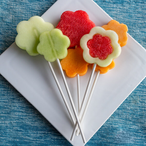 A plate of fruit skewers with paper chocolate roses on the ends.