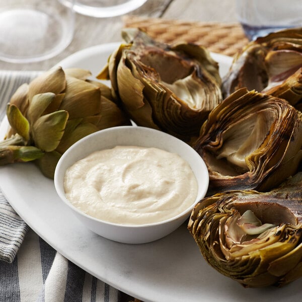 A plate of artichokes with a white bowl of garlic aioli for dipping.