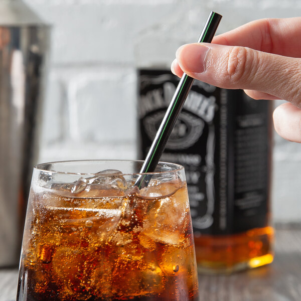 A hand holding an Eco-Products GreenStripe black cocktail straw in a glass of ice with a brown liquid.