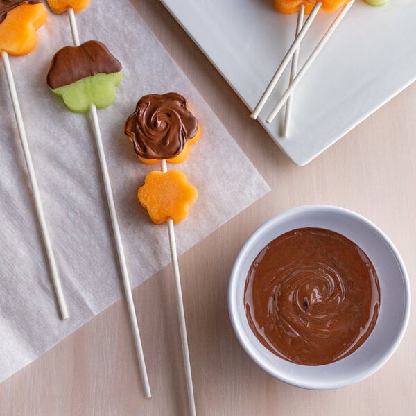 A plate of chocolate dipped fruit on paper rose sticks with chocolate sauce.