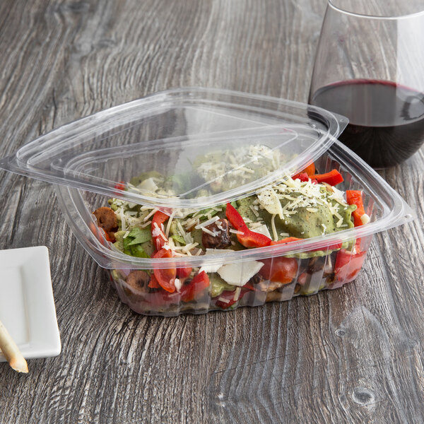 A salad in an Eco-Products rectangular deli container on a table with a glass of red wine.