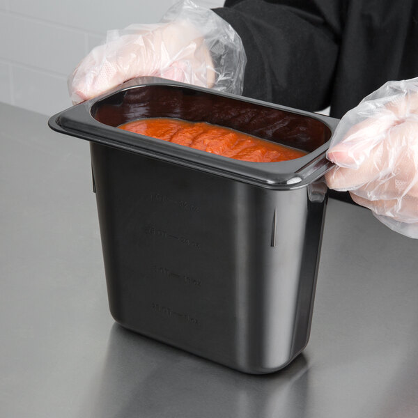 A person in gloves holding a Carlisle black plastic food pan full of food.