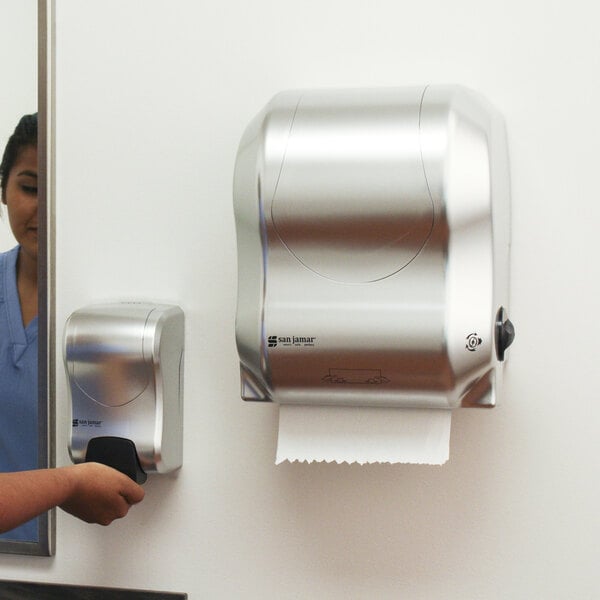 A woman in a blue shirt using the San Jamar Simplicity Essence Summit hands free paper towel dispenser.