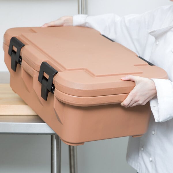 A woman holding a brown Cambro food pan carrier box.