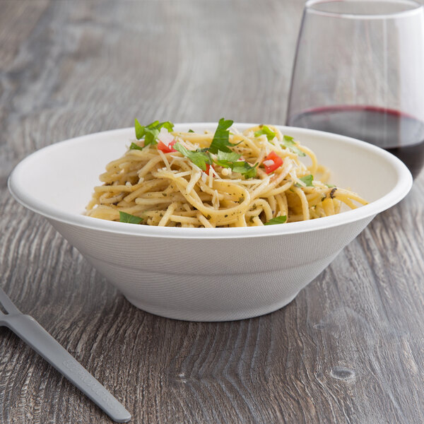 A white Eco-Products compostable noodle bowl filled with spaghetti and a glass of wine.