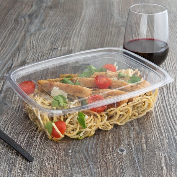 A rectangular Eco-Products deli container filled with pasta and tomatoes on a table with a glass of red wine.