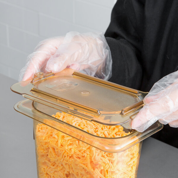 A person in gloves holding a Carlisle plastic container with shredded cheese.