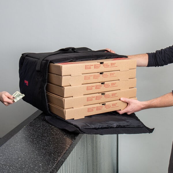 A man handing a stack of pizza boxes to a black Cambro Pizza Delivery GoBag.