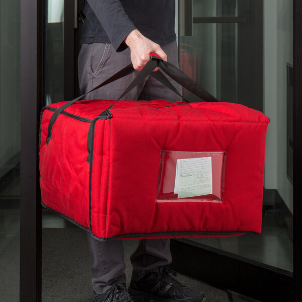 A person holding a red Cambro insulated pizza delivery bag with a clear window.