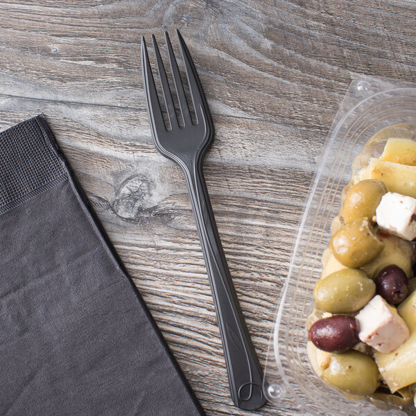 A plastic container of food next to a black compostable plastic fork.