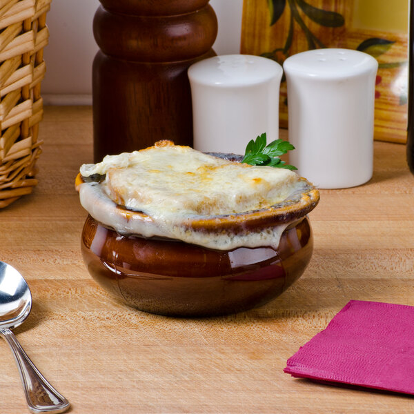 A close up of French onion soup in a brown Tuxton onion soup bowl with cheese on top.