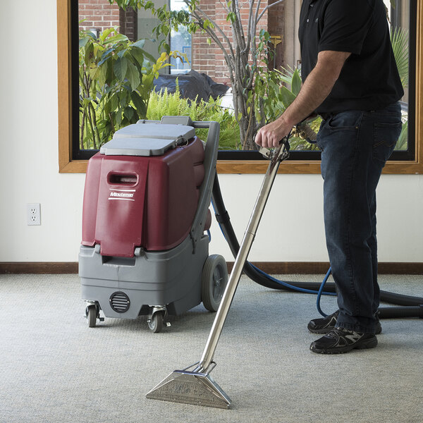 A man using a Minuteman Rush 100 carpet extractor to clean a carpet.