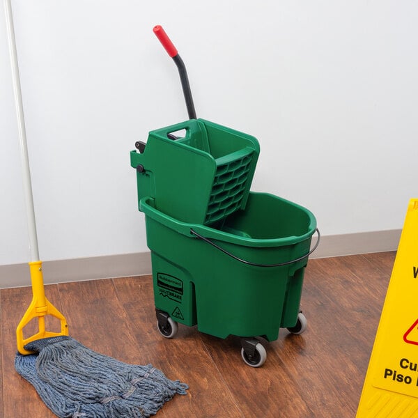 A green Rubbermaid WaveBrake mop bucket with wringer on a wood floor.