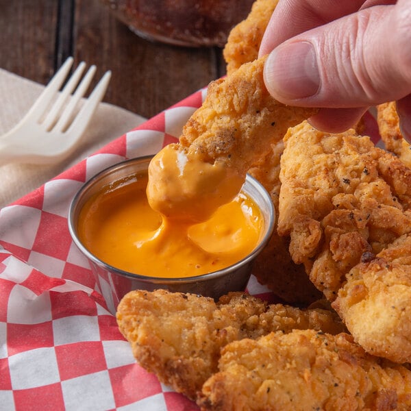 A person dipping a piece of fried chicken into a cup of Ken's Foods Boom Boom Sauce.