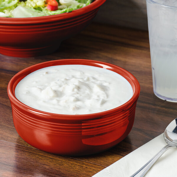 A Scarlet Fiesta chowder bowl filled with white liquid on a table with a salad.