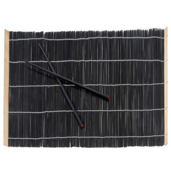 A pair of chopsticks on a black bamboo placemat.