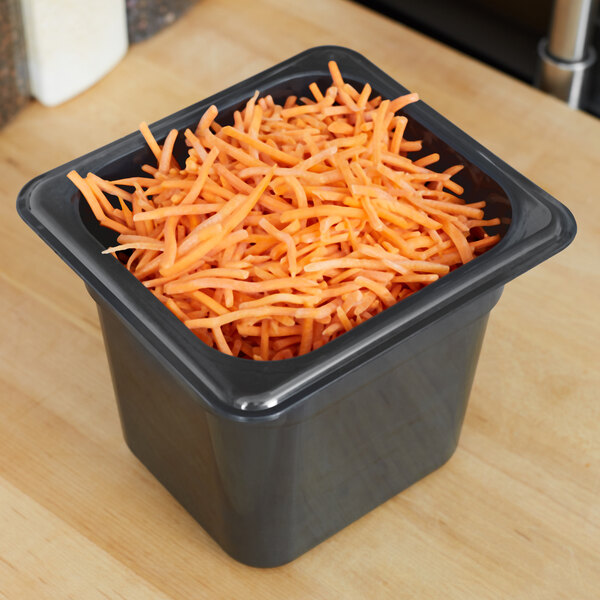 A black Cambro H-Pan filled with shredded carrots on a wooden counter.