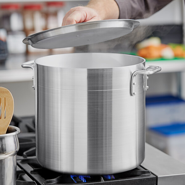 A person using a Choice 20 Qt. aluminum stock pot to cook food on a stove.