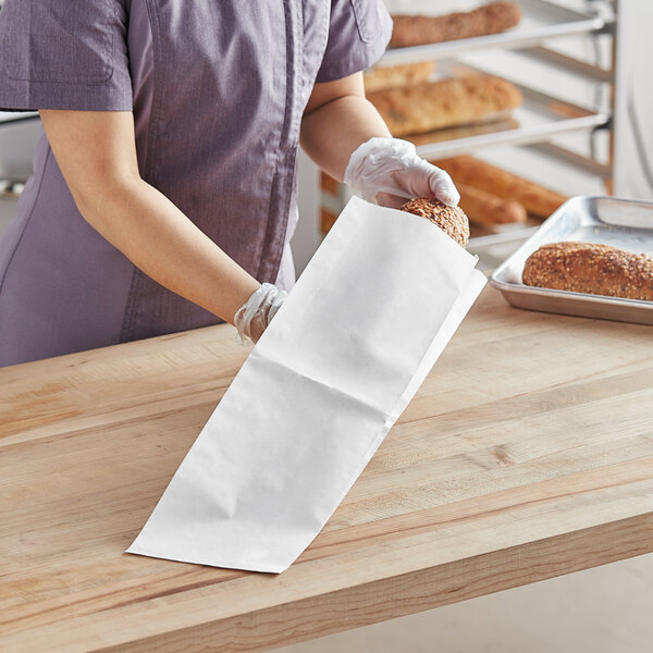 A person wearing gloves holding a plain white paper bread bag.