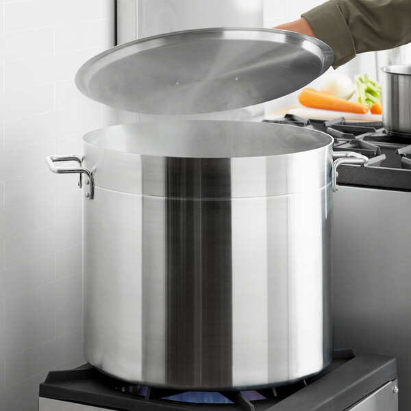 A person pouring from a large Choice aluminum stock pot on a stove.
