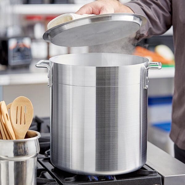 A person using a Choice aluminum stock pot and lid on a stove.