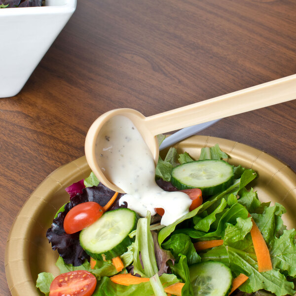A beige plastic Thunder Group ladle pouring dressing on a salad.