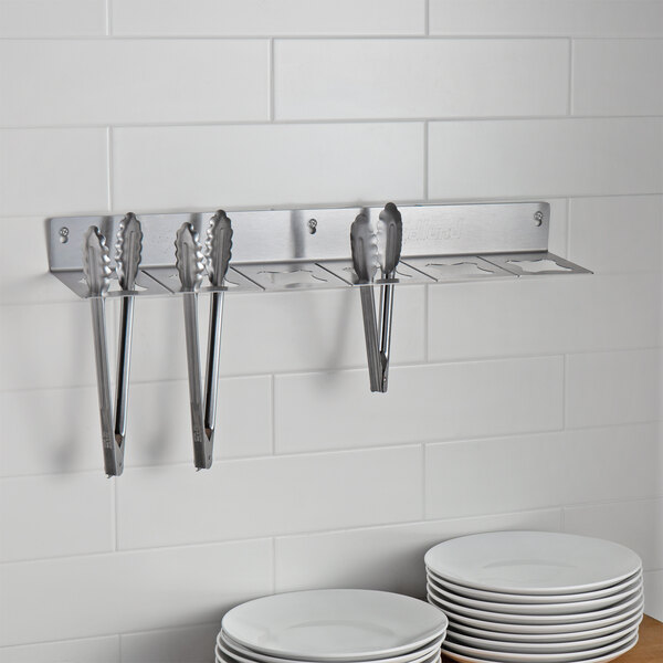 An Edlund Smart Tong Holder on a wall with tongs in it.