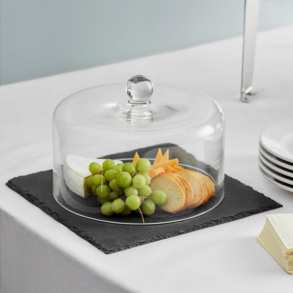 A glass dome on a black slate tray with food on it.